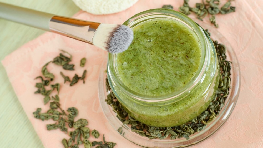 A green tea mask in a jar with a face brush next to it.